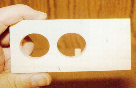wood board with two holes drilled in to it and a round peg pushed through visible in one of the holes